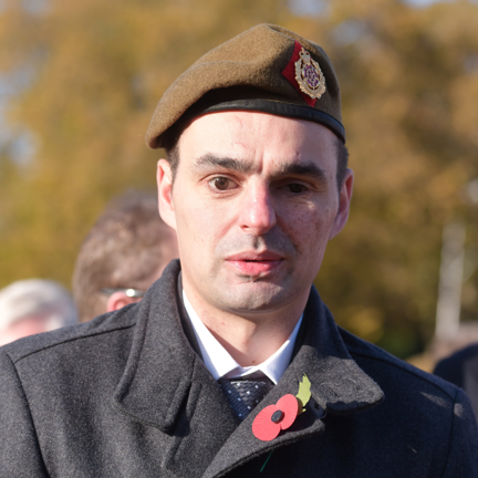 Craig dressed in a black coat with a poppy in his button hole and wearing a beret