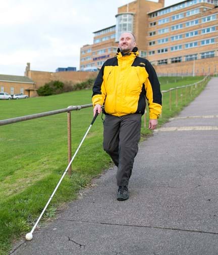 Blind veteran Mark using a guide cane to walk down a path in front of Blind Veterans UK centre of wellbeing
