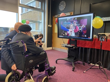 Blind veteran Ken in front of a TV screen with Margaret waving from the video call