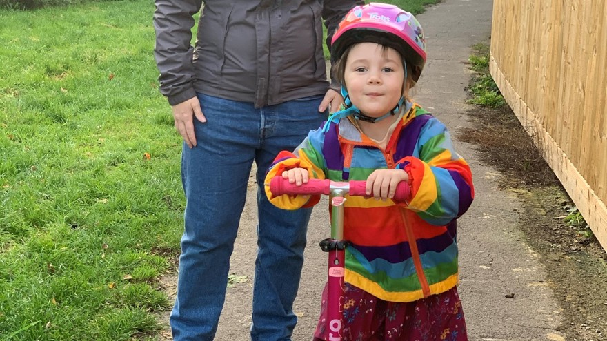 Blind veteran Kelly outside with her daughter Bethany who is riding a scooter