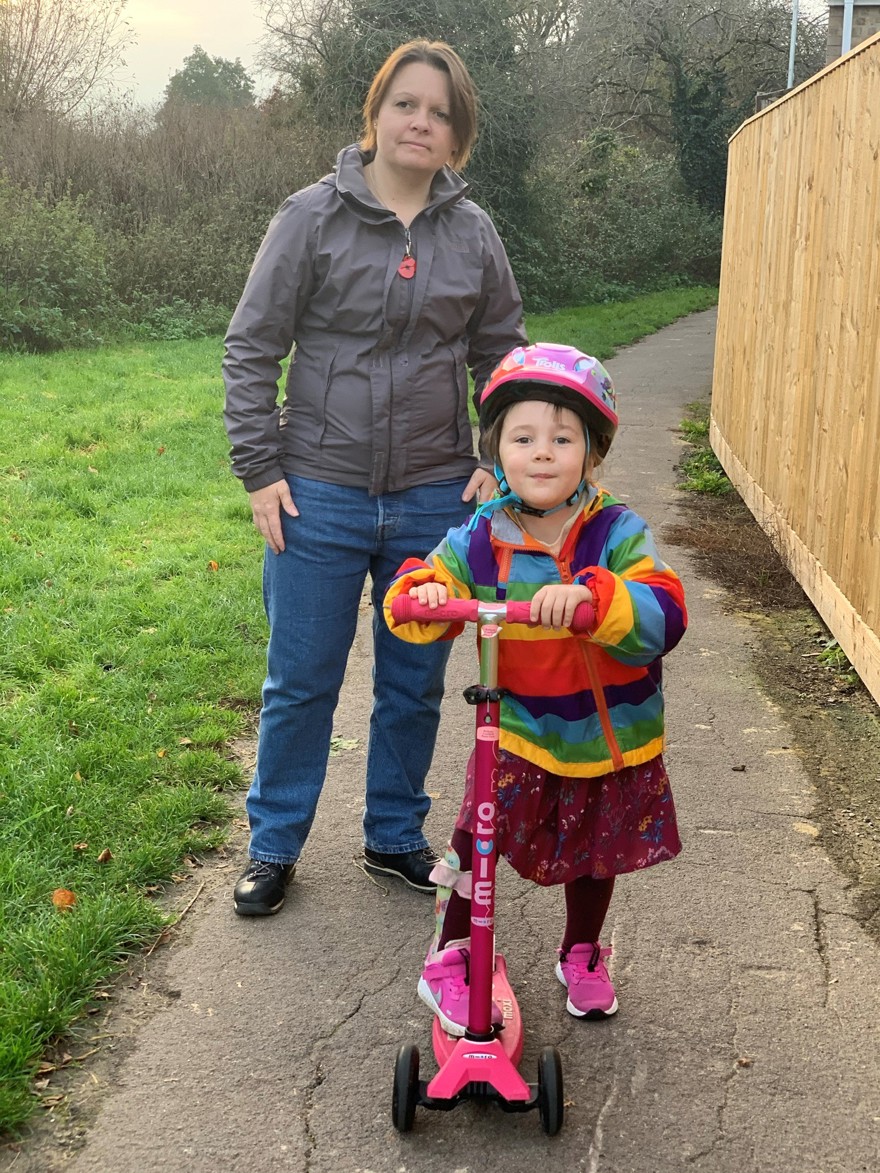Blind veteran Kelly outside with her daughter Bethany who is riding a scooter