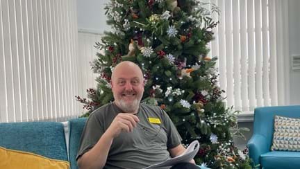 A man sat in an armchair in front of a Christmas tree