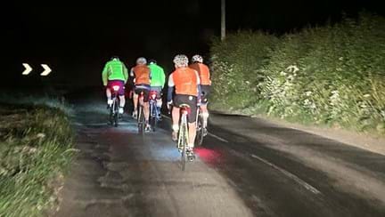 Image from behind the cyclists, who are all wearing high vis tops, as they ride along a road in the dark
