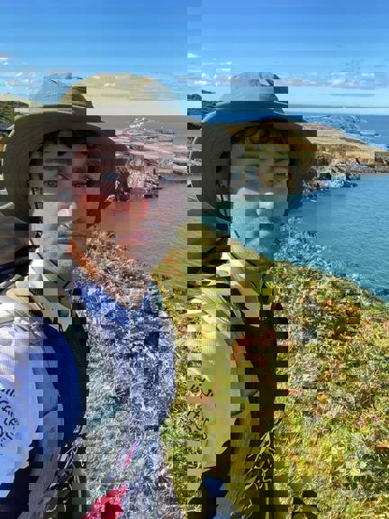 James wearing a Blind Veterans UK t shirt stood on the coastal path on a very sunny day with the sea in the background