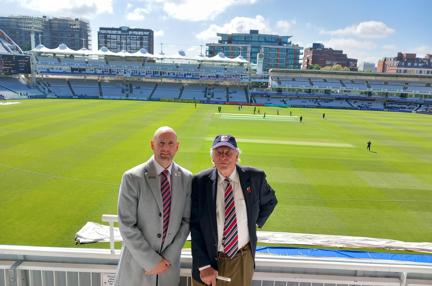 Chris and Tim stood side by side with play taking place on the cricket pitch behind them