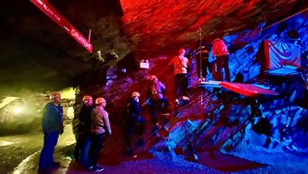A darkly lit cavern in an old slate mine, with a group of eight blind veterans and Blind Veterans UK staff wearing helmets and harnesses as they practice climbing.