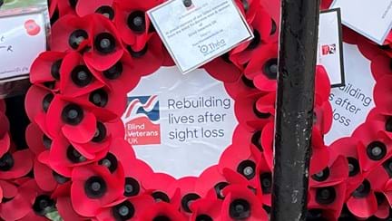 Close up of poppy wreath with Blind Veterans UK logo in the centre and a label attached which reads "In proud memory of our fallen comrades from the blind ex-Service men and women of Blind Veterans UK gifted by Thea Pharmaceuticals