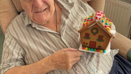 Blind veteran Maurice looks into the camera and smiles while holding a small gingerbread house