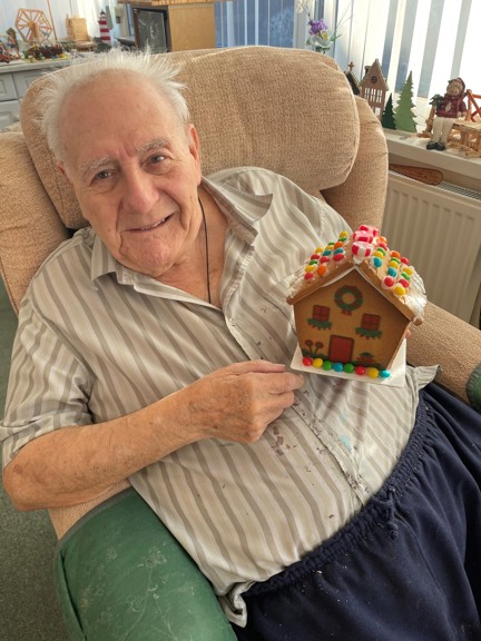 Blind veteran Maurice looks into the camera and smiles while holding a small gingerbread house