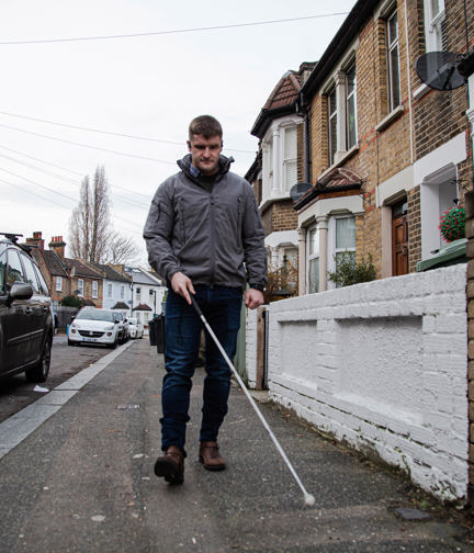 Photo of blind veteran Rob walking down the street using a guide cane