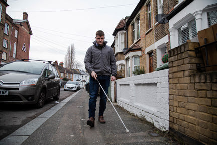 Photo of blind veteran Rob walking down the street using a guide cane