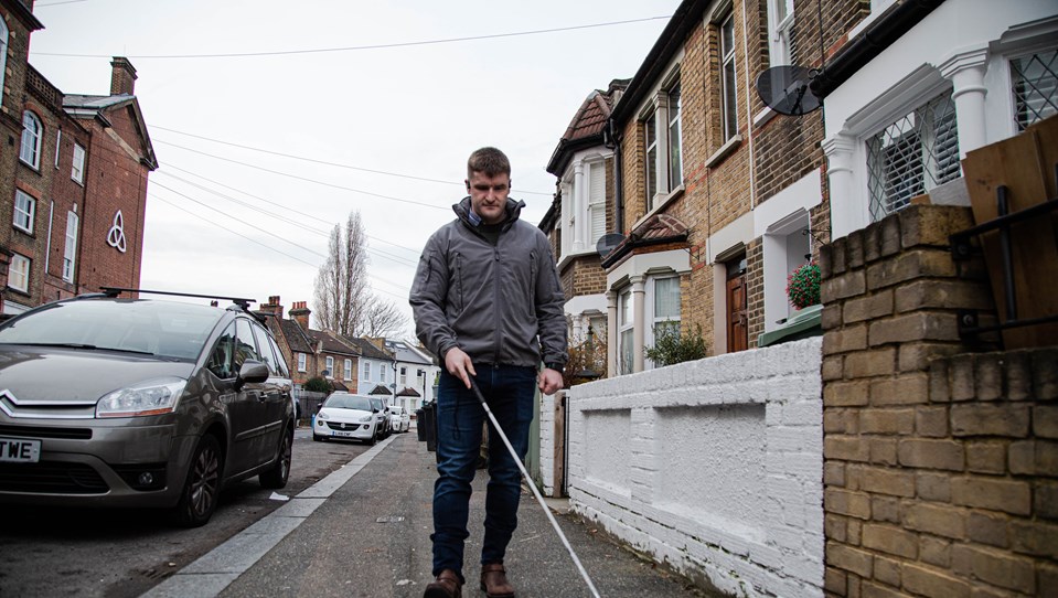 Photo of blind veteran Rob walking down the street using a guide cane
