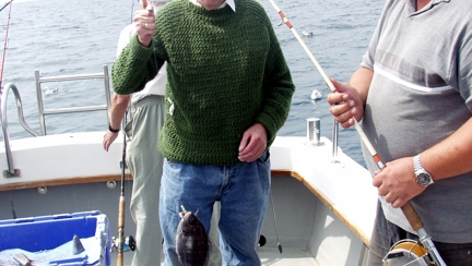 Blind veteran Fred standing on a boat next to a man who has caught a fish, giving a thumbs up