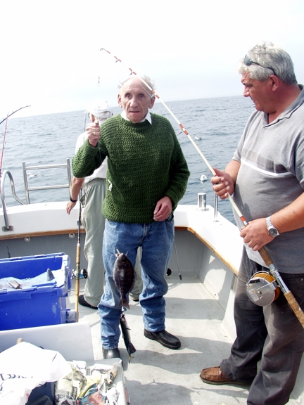 Blind veteran Fred standing on a boat next to a man who has caught a fish, giving a thumbs up
