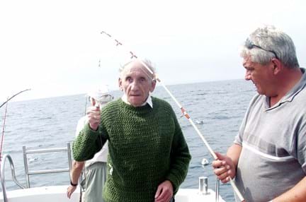 Blind veteran Fred standing on a boat next to a man who has caught a fish, giving a thumbs up