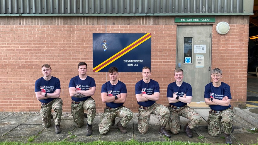 A group of supporters, kneeling, wearing matching army trousers and Blind Veterans UK t-shirts