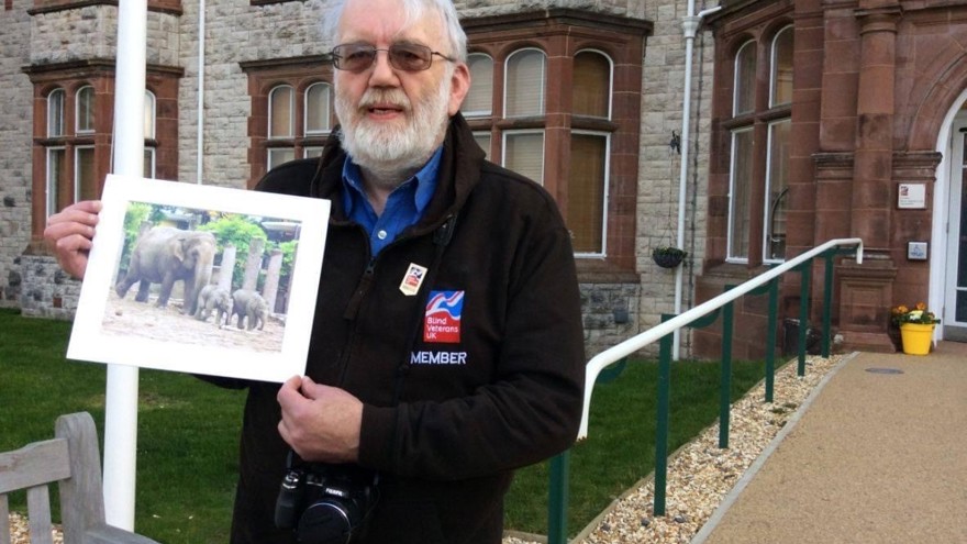 A photo of blind veteran Barrie holding up one of his photographs of an elephant and its calves