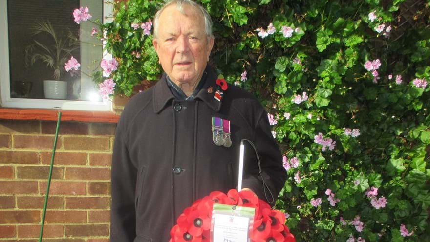 Blind Veteran Jim stood in his garden wearing a poppy and displaying his medals. He is holding his white cane and his poppy wreath.