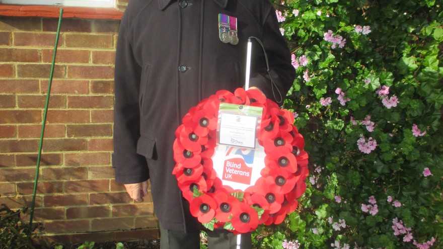 Blind Veteran Jim stood in his garden wearing a poppy and displaying his medals. He is holding his white cane and his poppy wreath.