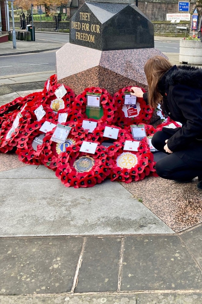 Stephanie wearing a black coat and kneeling down to place a wreath at the memorial