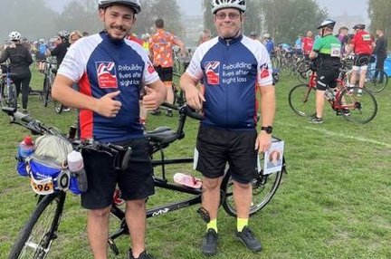 Blind veteran Andy and his son, in Blind Veterans UK cycling tops, stood next to their tandem bicycle