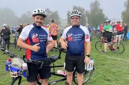 Blind veteran Andy and his son, in Blind Veterans UK cycling tops, stood next to their tandem bicycle
