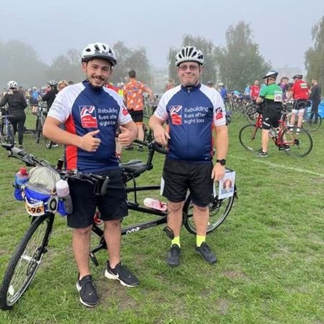 Blind veteran Andy and his son, in Blind Veterans UK cycling tops, stood next to their tandem bicycle