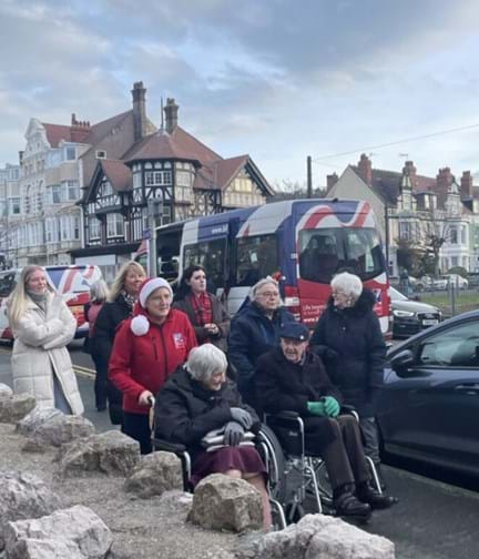 Blind veterans gathered outside a Blind Veterans UK van, some standing and some are in wheelchairs being supported by staff