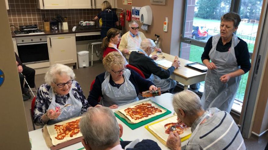 A group of blind veterans adding toppings to their pizza