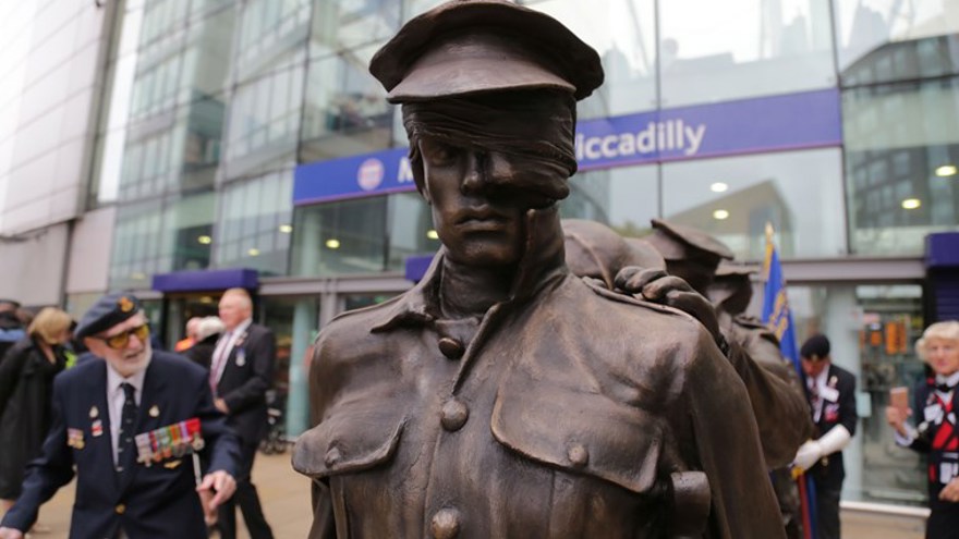 A close up photo of the Victory Over Blindess statue with blind veteran Jim in the background