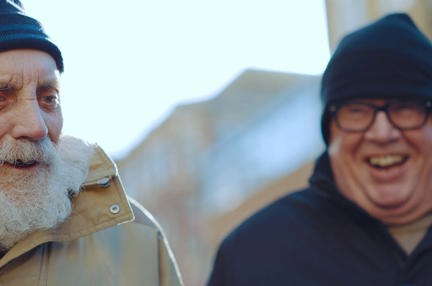 Blind veteran Ken and volunteer Liam laughing as they walk together outside, both wrapped up warm in winter clothing