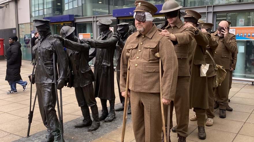 Seven men dressed in First World War army uniforms stand next to the statue of the same style