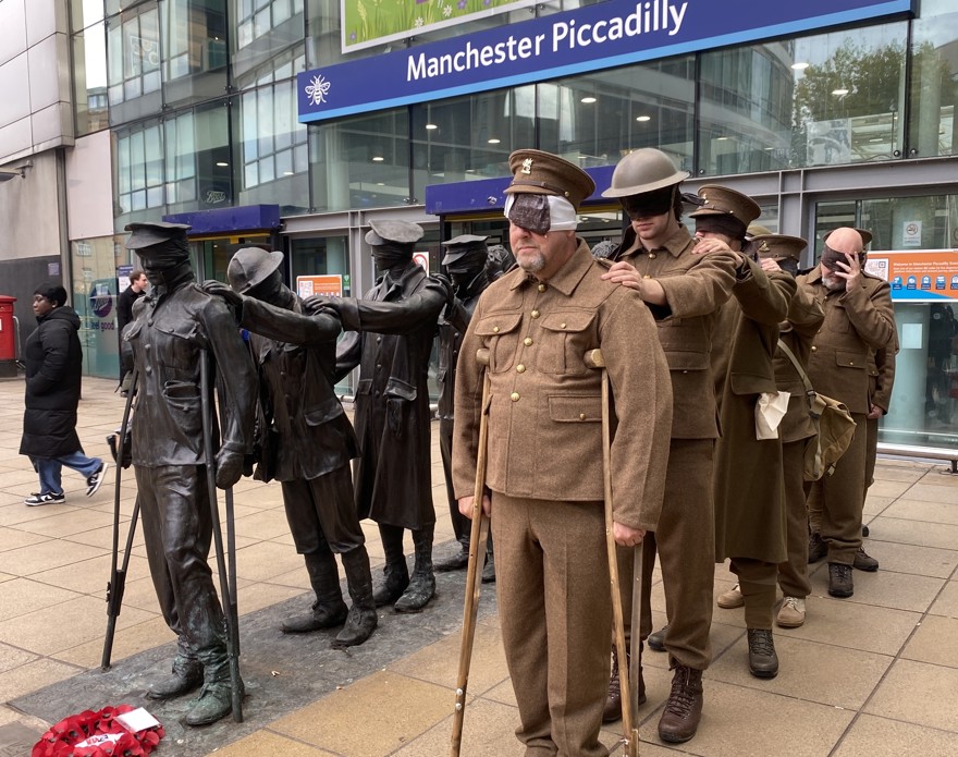 Seven men dressed in First World War army uniforms stand next to the statue of the same style