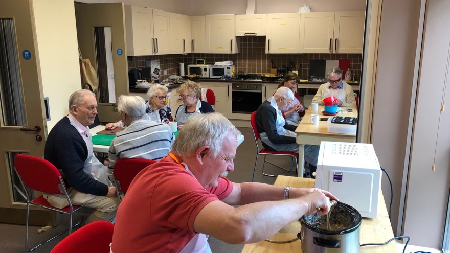 Blind veterans sitting in a kitchen around tables, using a slow cooker