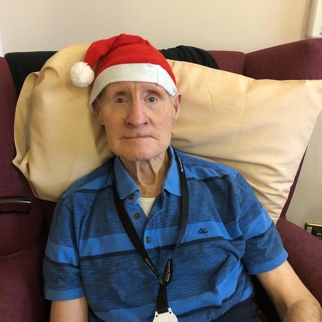 Blind veteran Arthur sitting down on an armchair, wearing a Christmas hat