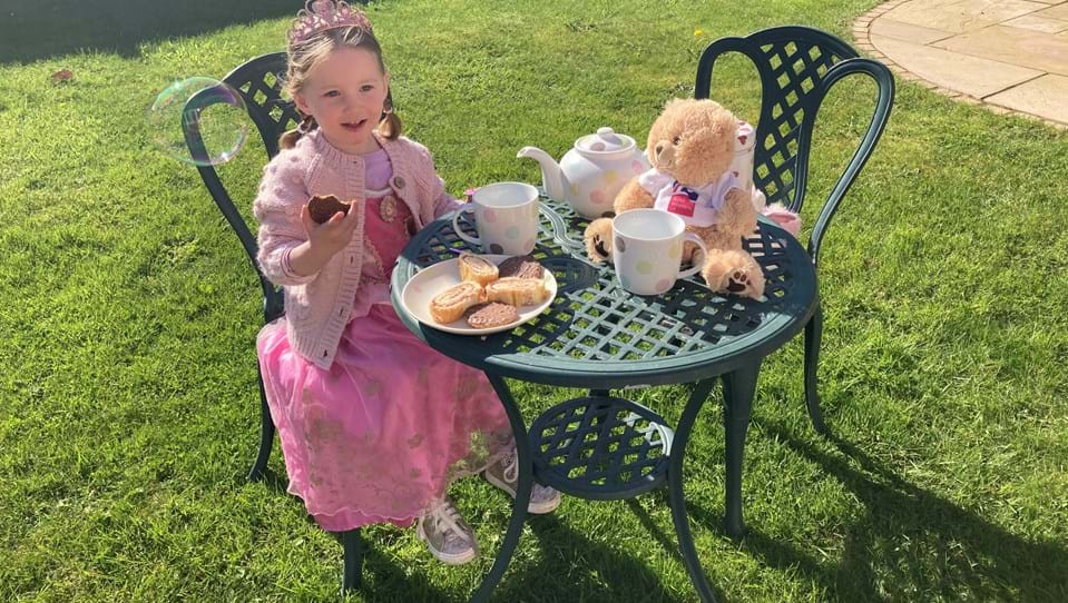 Little girl dressed as a princess enjoying a Brew Up tea party with her teddy.  Ted is wearing a Blind Veterans UK T-shirt.