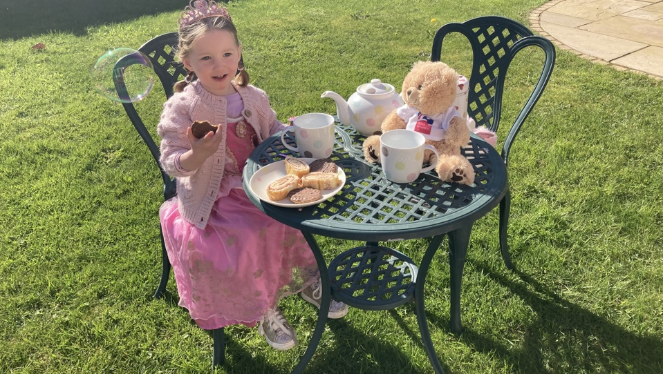 Little girl dressed as a princess enjoying a Brew Up tea party with her teddy. Ted is wearing a Blind Veterans UK T-shirt.