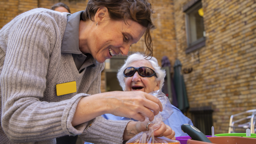 Blind veteran Connie, wearing dark sunglasses and laughing as she speaks to Blind Veterans UK staff member