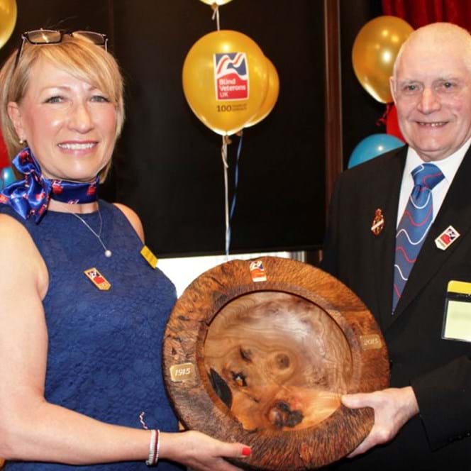 Blind veteran Bill and social worker Elizabeth smiling as they hold a wooden carved bowl