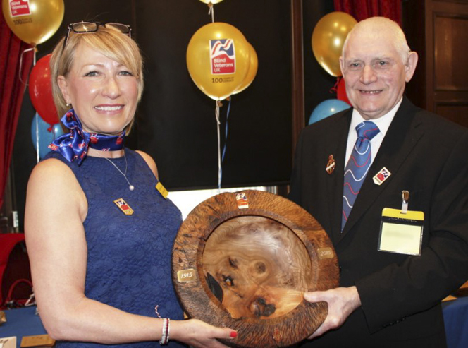 Blind veteran Bill and social worker Elizabeth smiling as they hold a wooden carved bowl