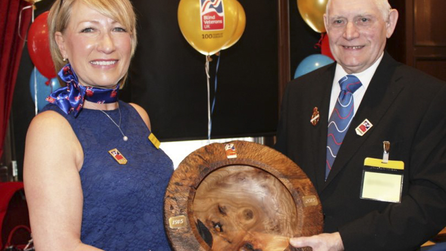 Blind veteran Bill and social worker Elizabeth smiling as they hold a wooden carved bowl