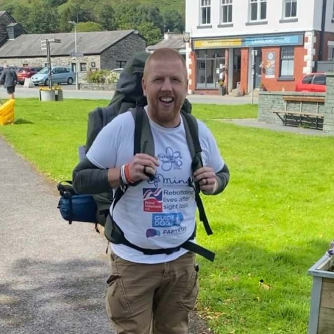 Charity supporter Stacey wearing a large backpack, walking gear and charity t-shirt, smiling as he walks
