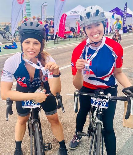 Maria and Sigil astride their bikes, smiling and holding their medals proudly at the finish line