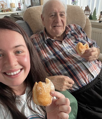 Blind veteran Maurice and volunteer Mia both hold a doughnut while smiling and looking into the camera