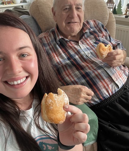 Blind veteran Maurice and volunteer Mia both hold a doughnut while smiling and looking into the camera