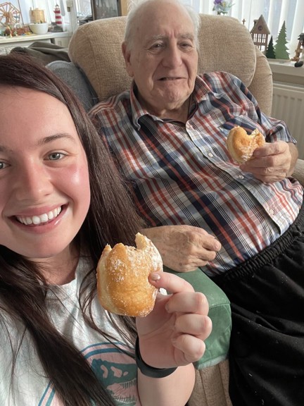 Blind veteran Maurice and volunteer Mia both hold a doughnut while smiling and looking into the camera