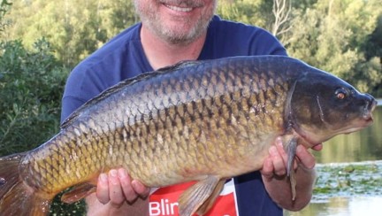 Mark kneeling down by the water holding a large carp in his hands