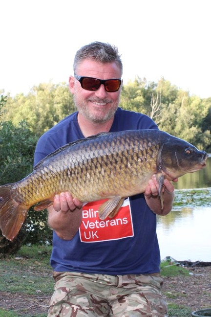 Mark kneeling down by the water holding a large carp in his hands