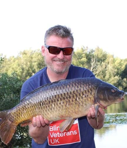 Mark kneeling down by the water holding a large carp in his hands