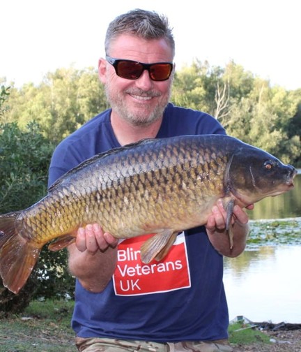 Mark kneeling down by the water holding a large carp in his hands